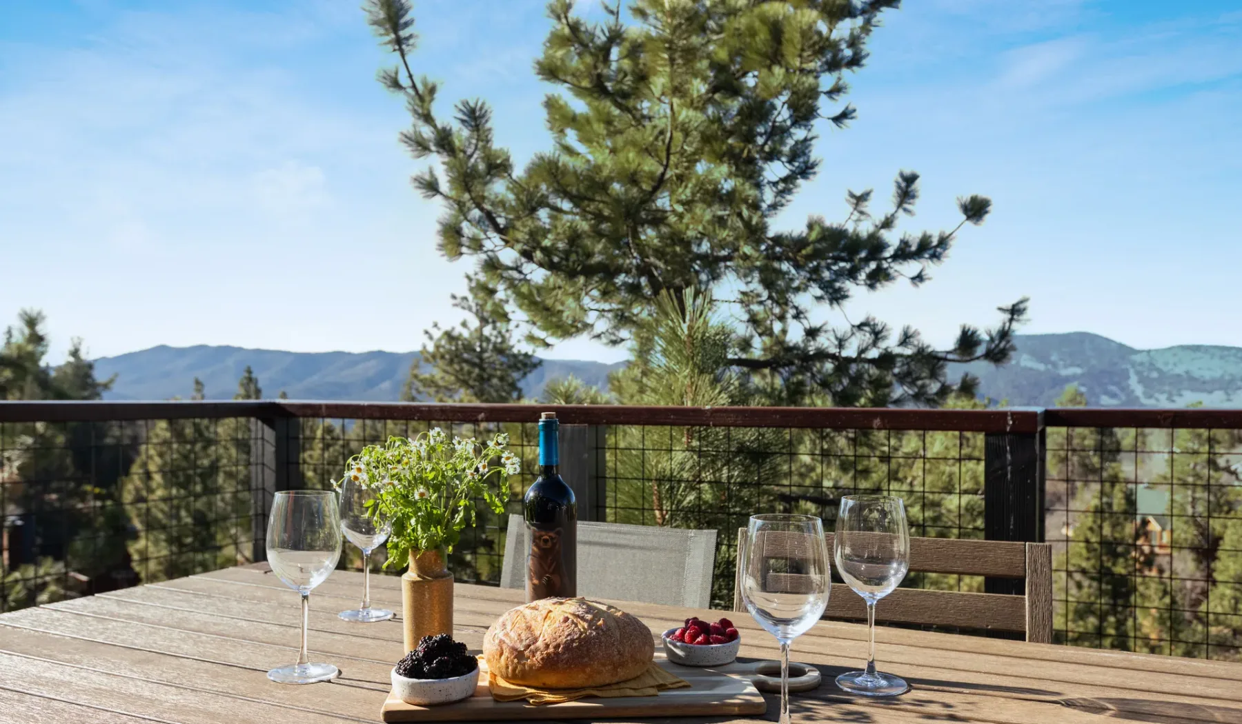 Una mesa de comedor al aire libre con pan y vino da a un paisaje montañoso.