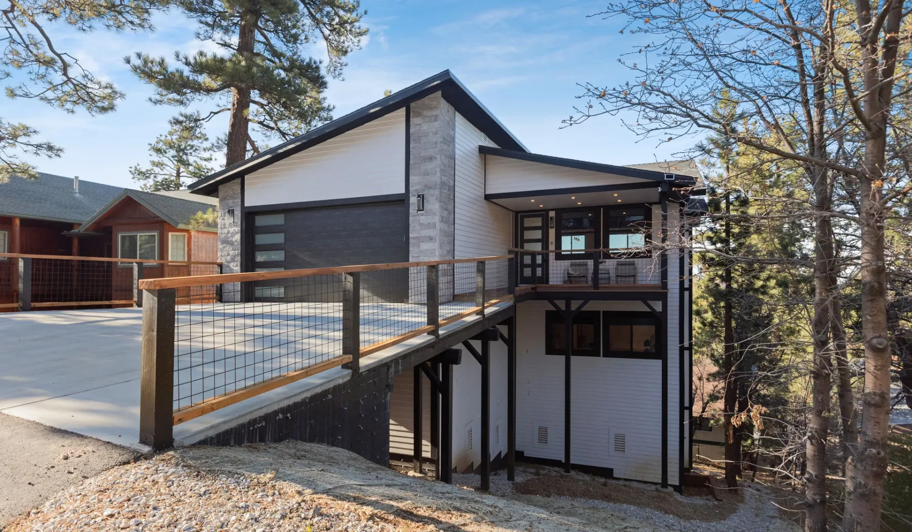 Una casa moderna está entre árboles, con un pasillo elevado que lleva a la entrada.