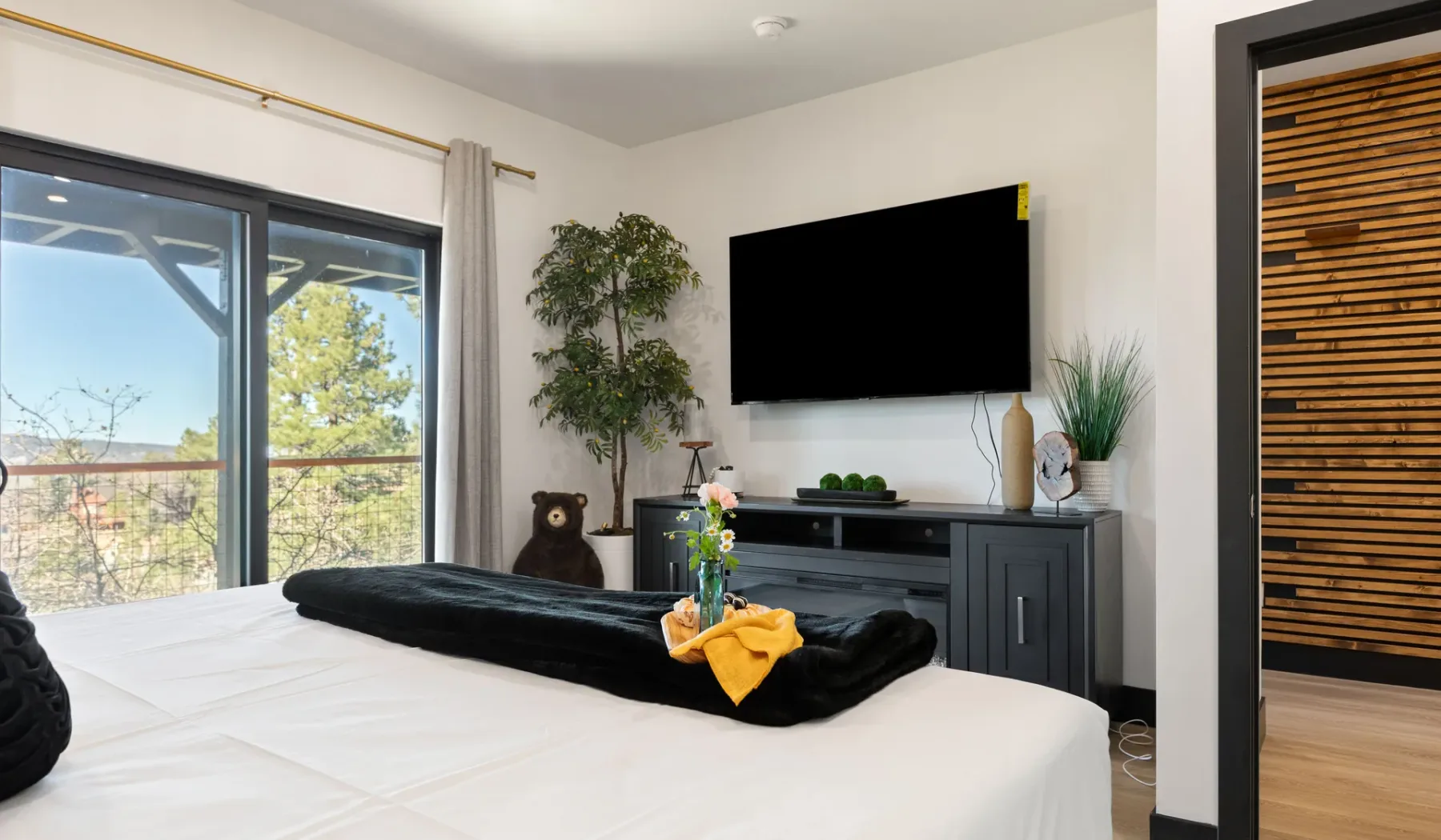 Un dormitorio con una cama frente a un televisor montado en la pared y un mueble oscuro.