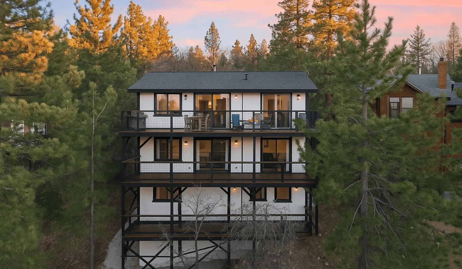 Una casa de varios niveles con balcones está entre árboles bajo un cielo rosado al atardecer.