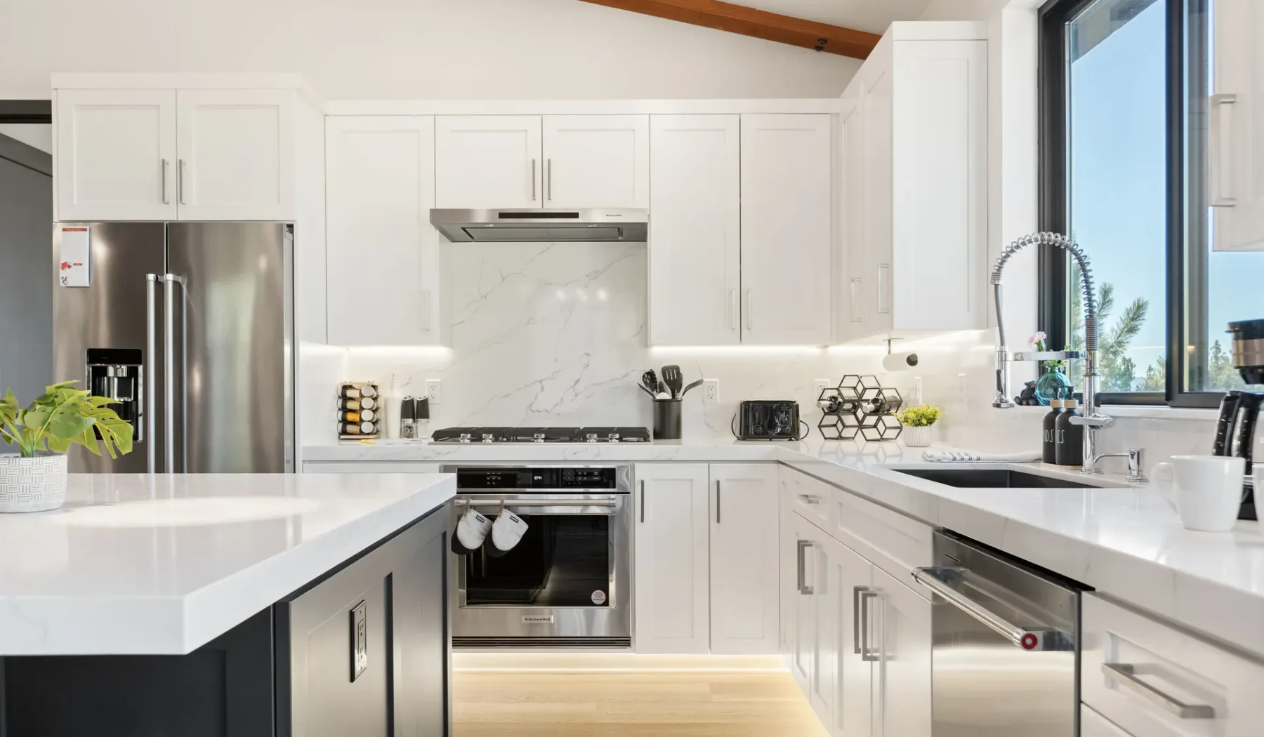 Una cocina moderna y luminosa con armarios blancos, electrodomésticos de acero inoxidable y una ventana grande.