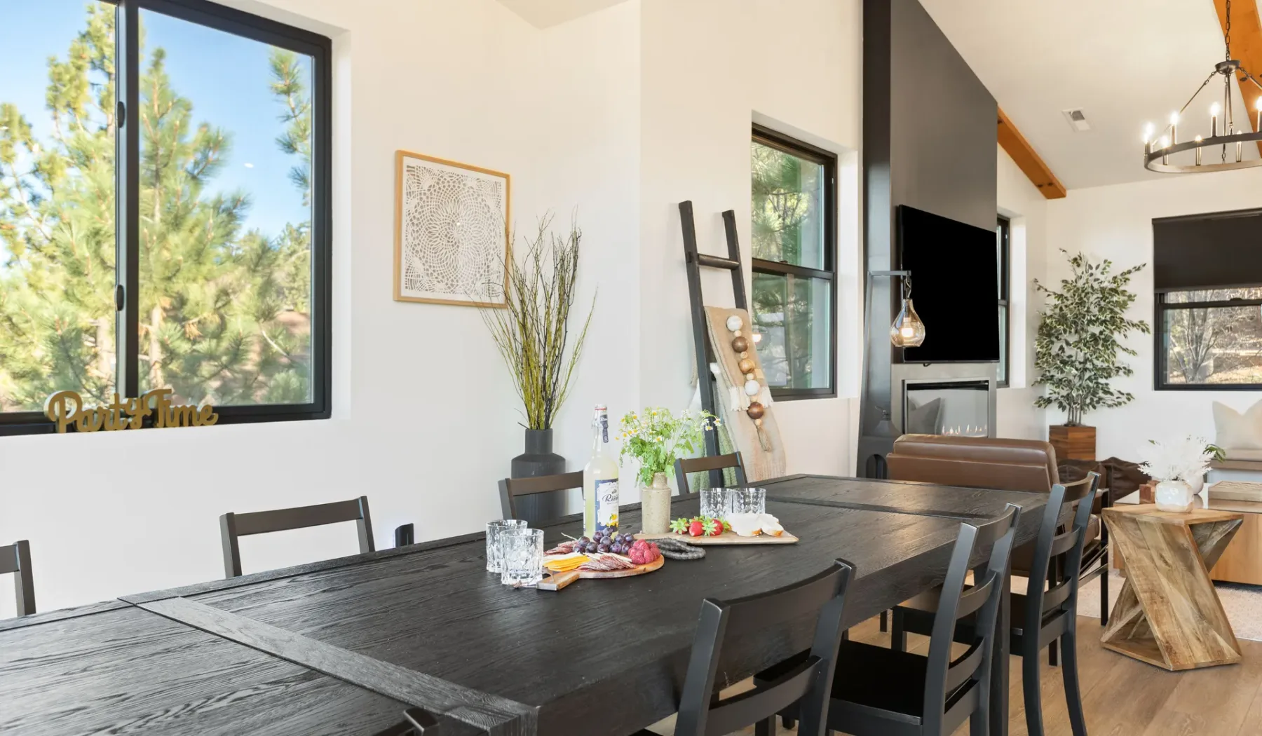 Un comedor con una mesa oscura y larga y grandes ventanas con vistas a los árboles.