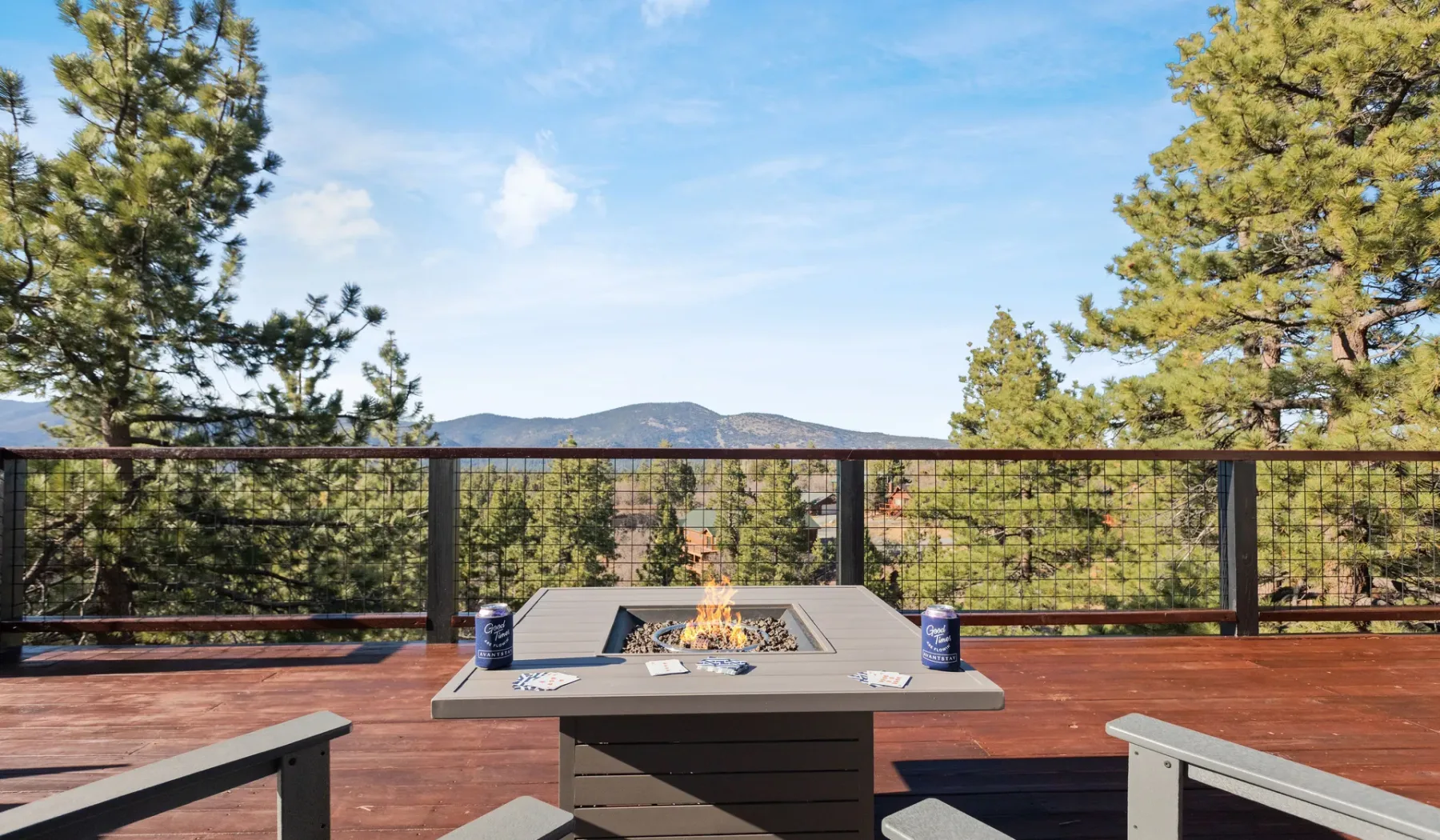 Una terraza de madera tiene una fogata y vistas de árboles y colinas lejanas.