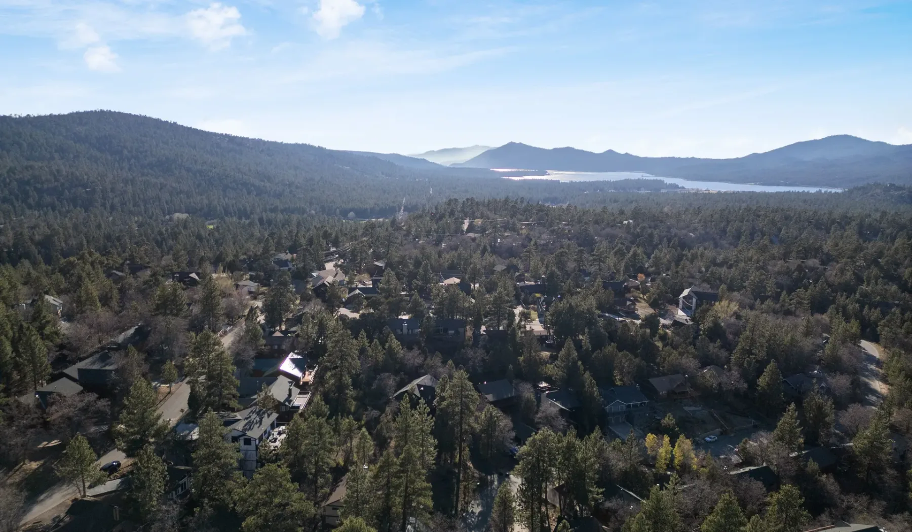 Vista aérea de un pueblo arbolado con colinas y un lago a lo lejos.