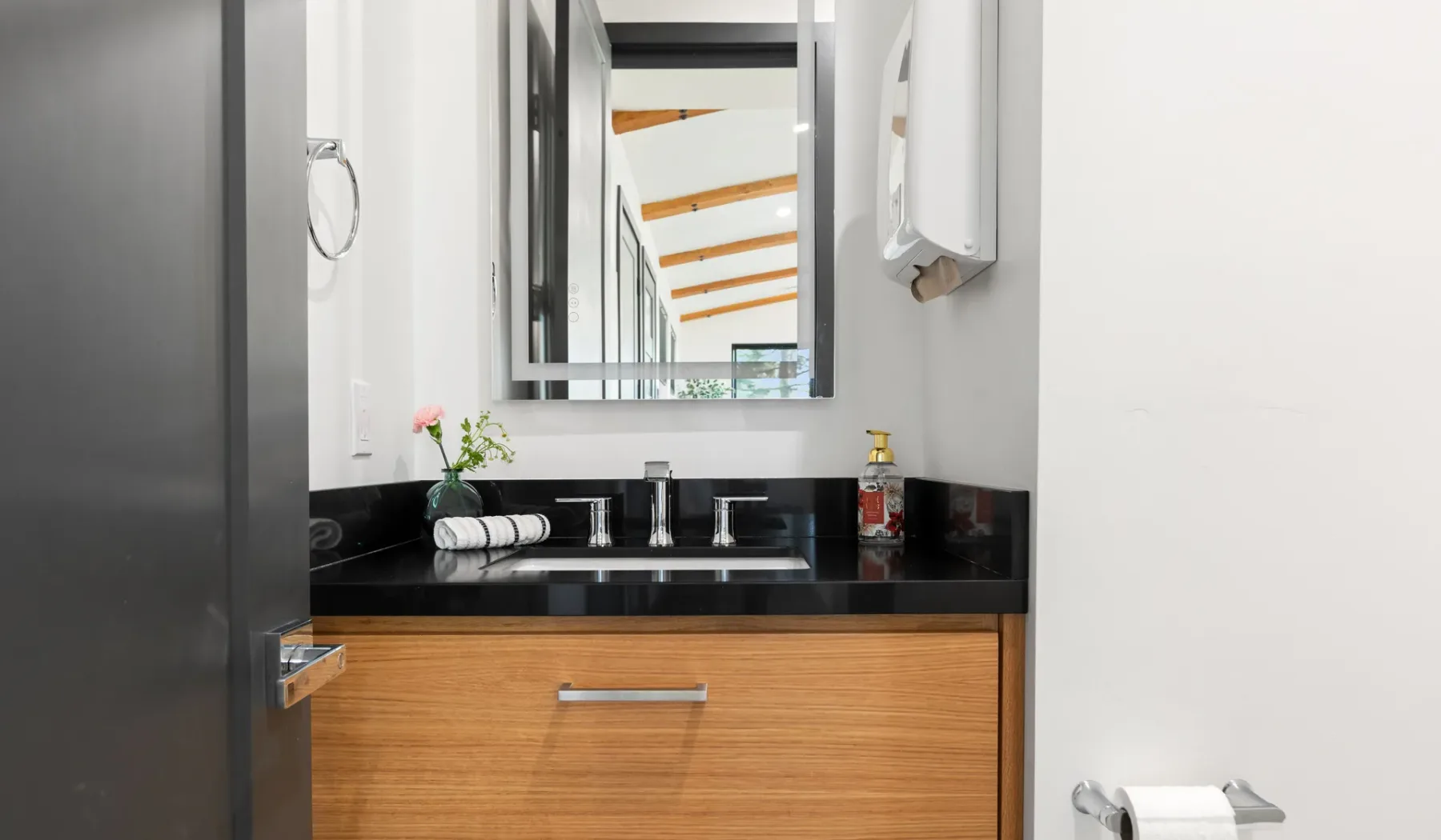 Un lavabo de baño con un espejo sobre una encimera negra.