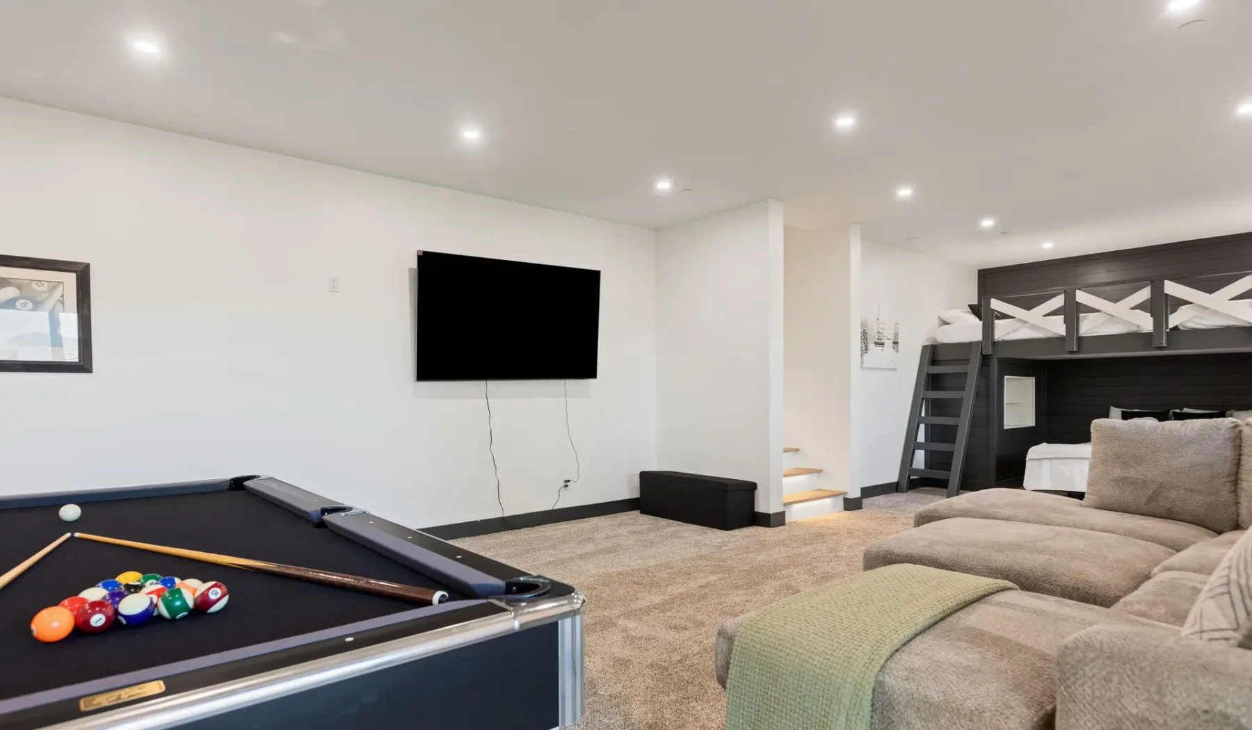 Una sala de recreación en el sótano tiene una mesa de billar, un televisor en la pared y asientos.