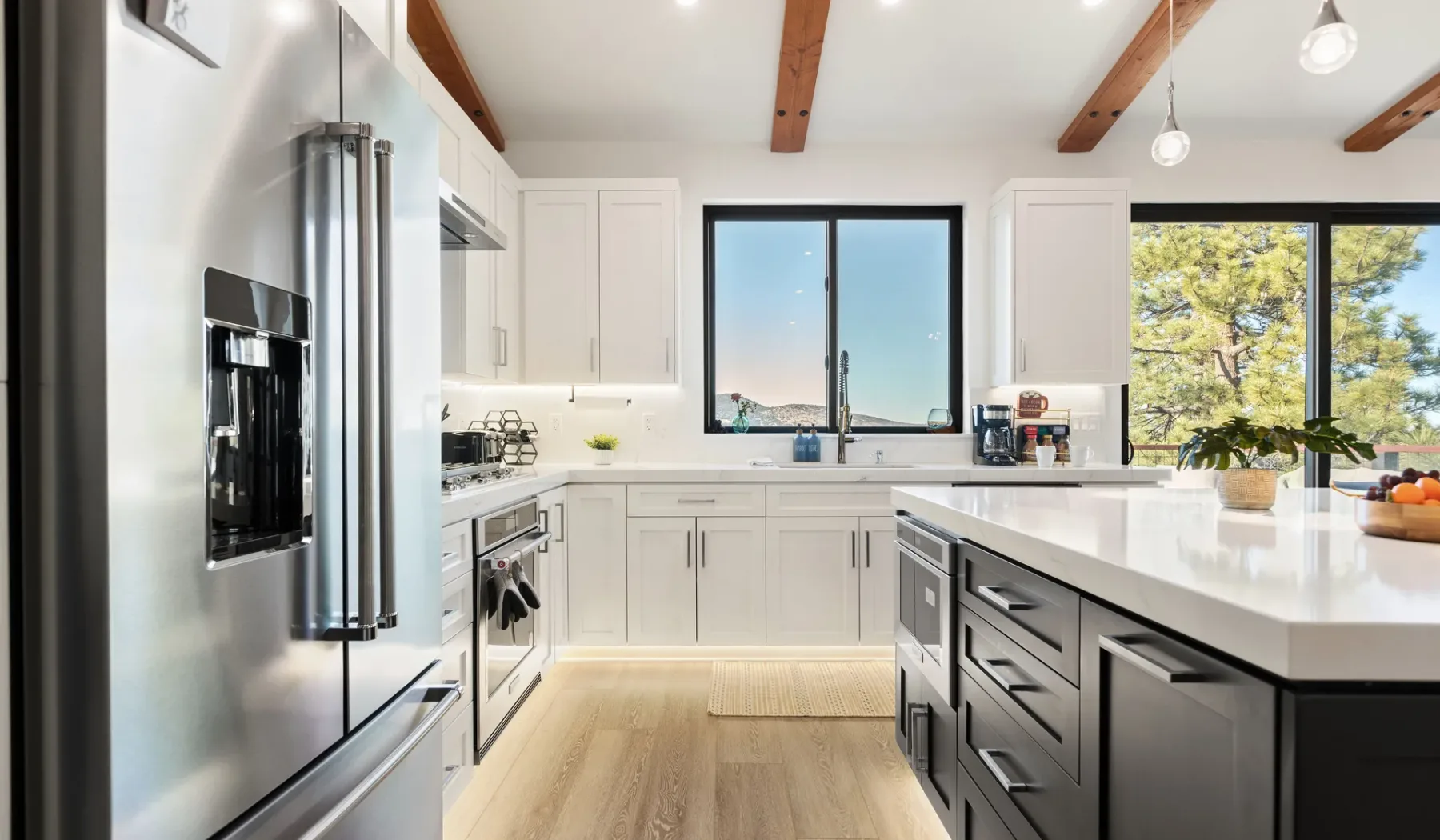 Una cocina luminosa con gabinetes blancos, encimeras oscuras y grandes ventanas.
