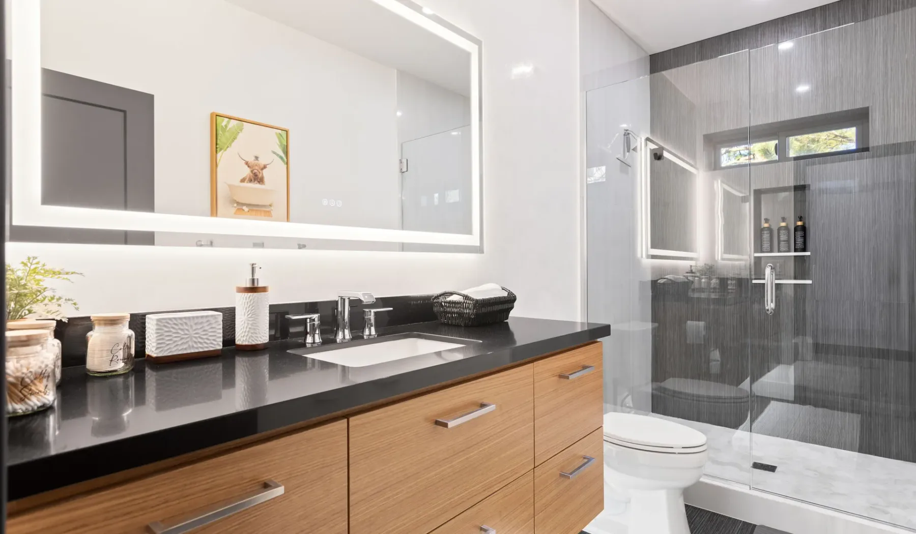 Un baño moderno cuenta con un largo tocador con lavabo junto a una ducha de vidrio.