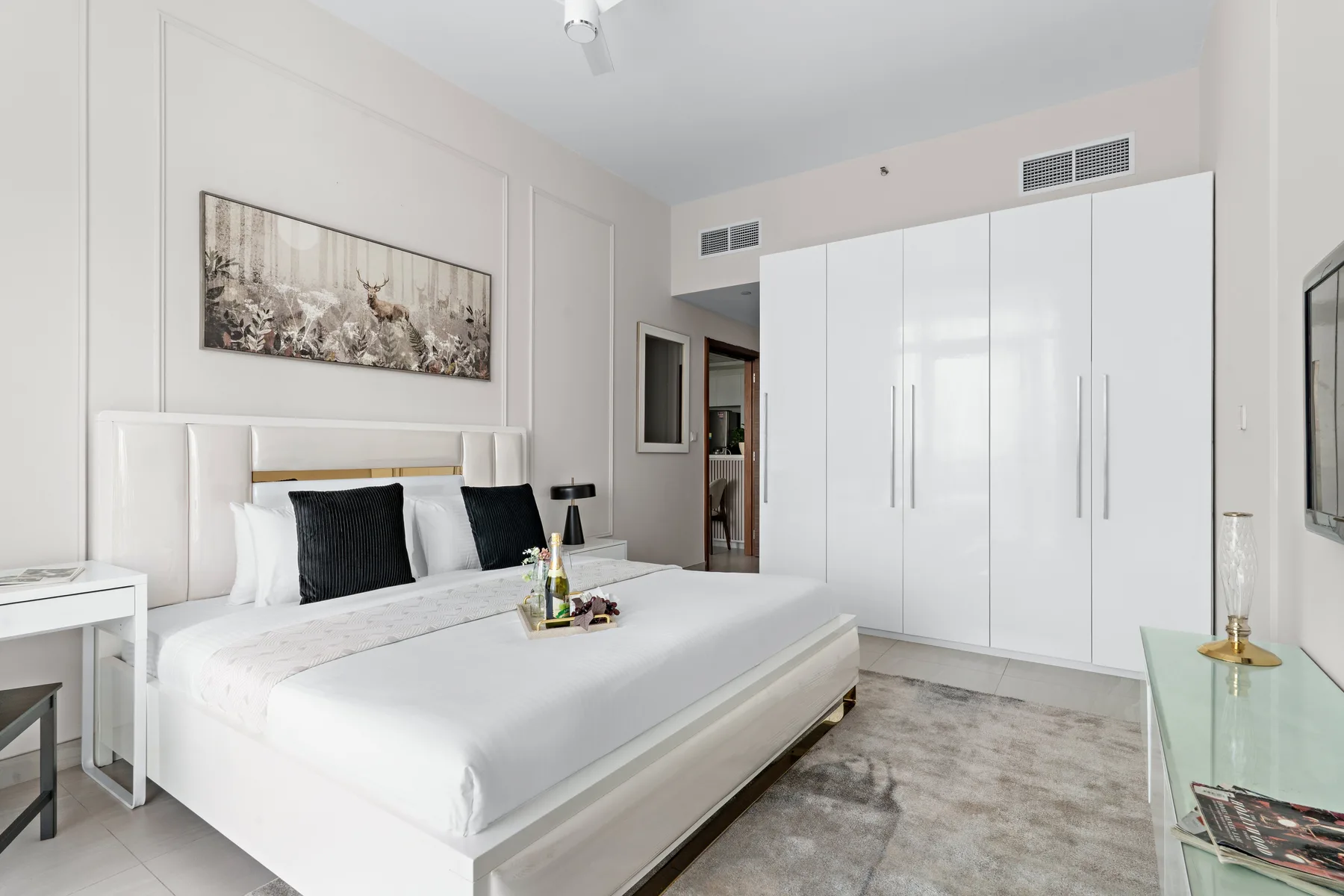 A bright bedroom features a white bed and large built-in wardrobes.