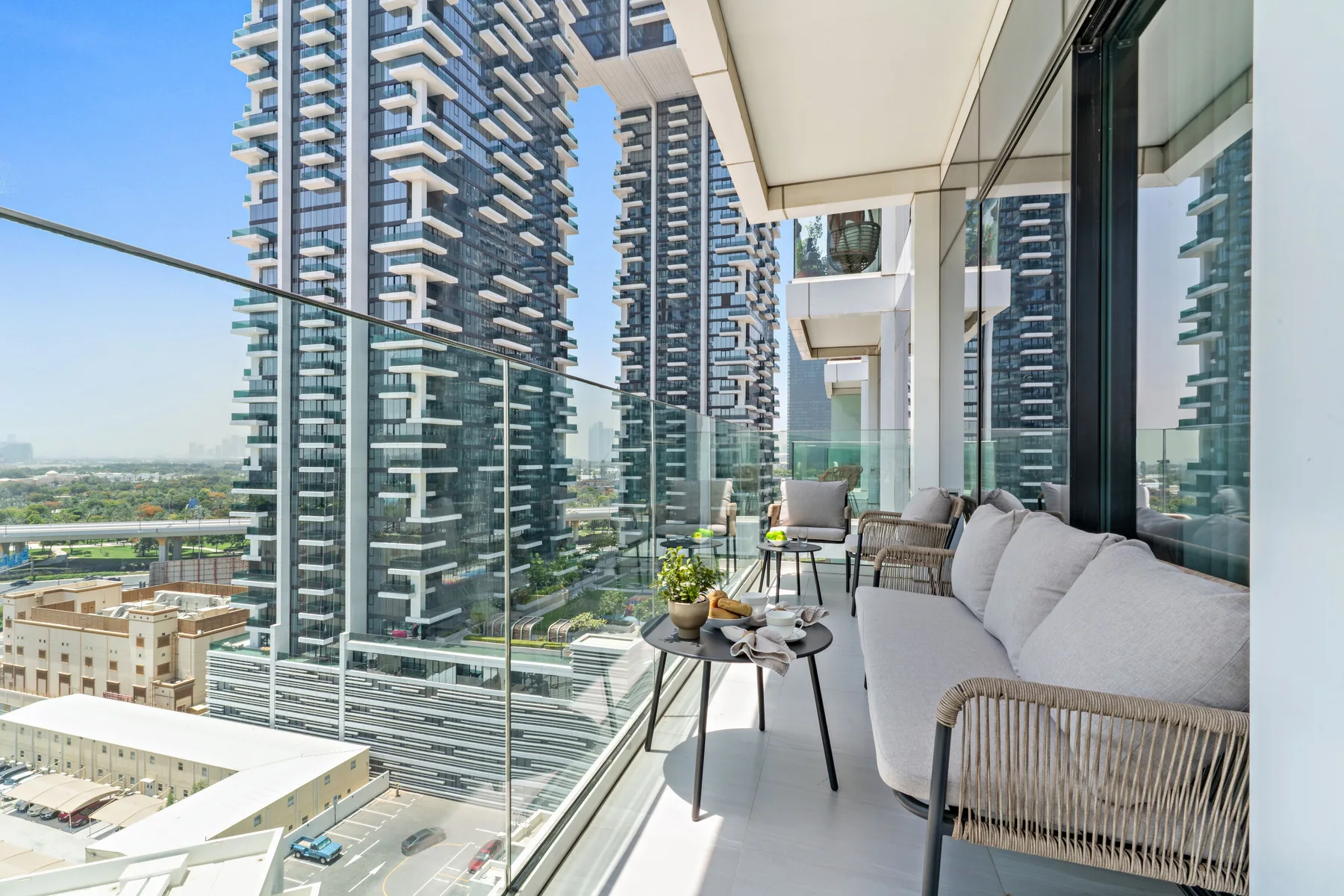 A high-rise balcony with seating and glass railings overlooks nearby towers.