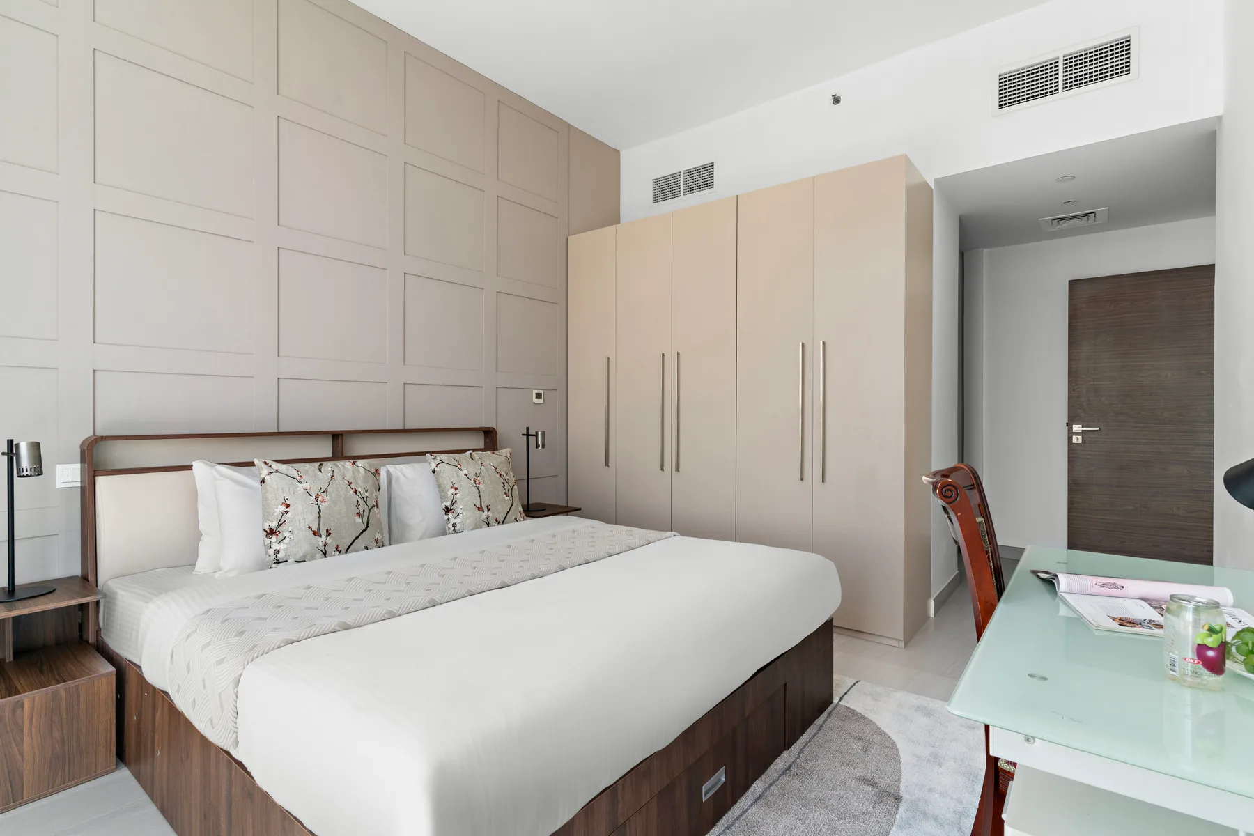 A bedroom with a bed, tall wardrobes, and a glass-topped desk.
