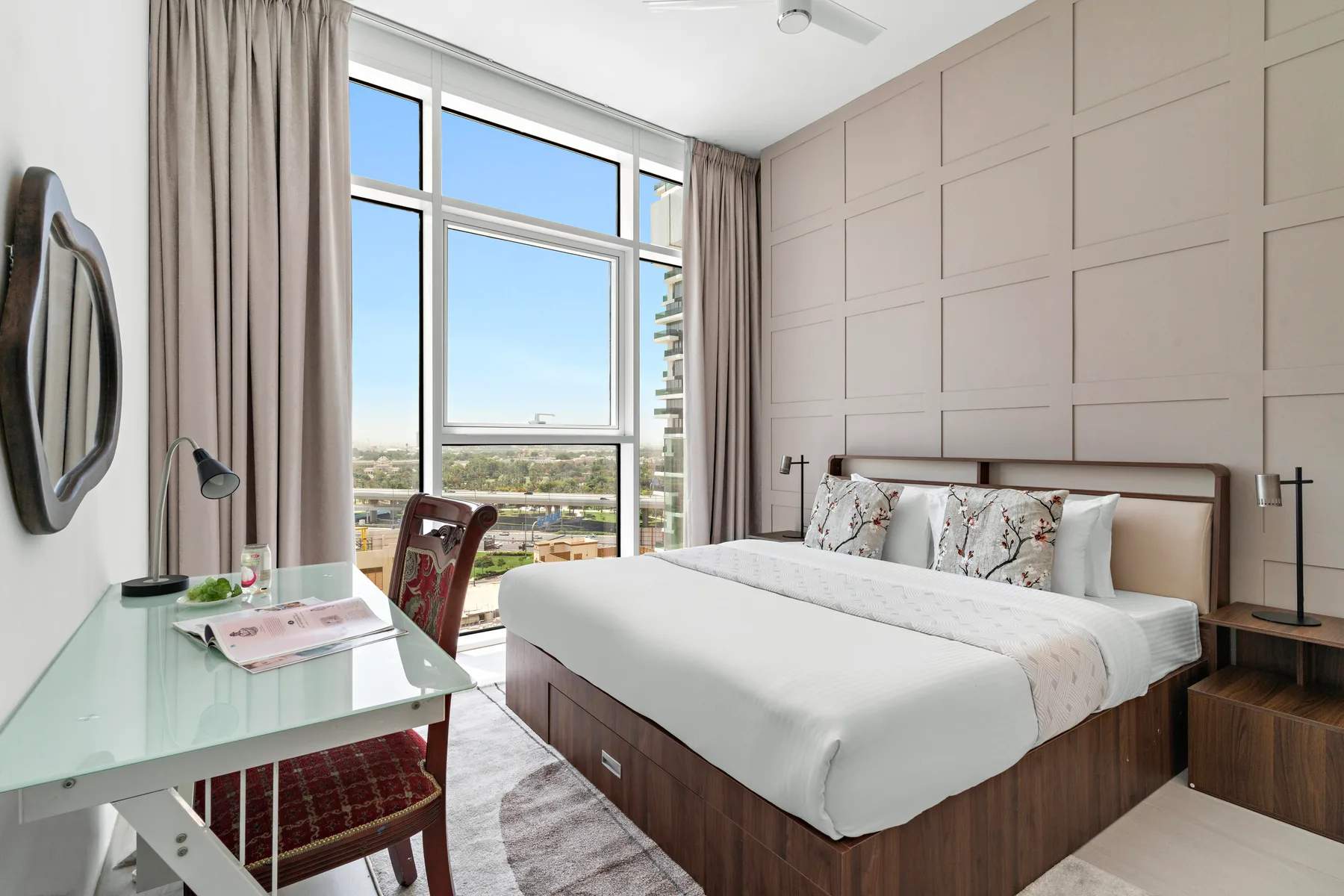 A bedroom with a bed, bedside tables, and large windows overlooking the city.
