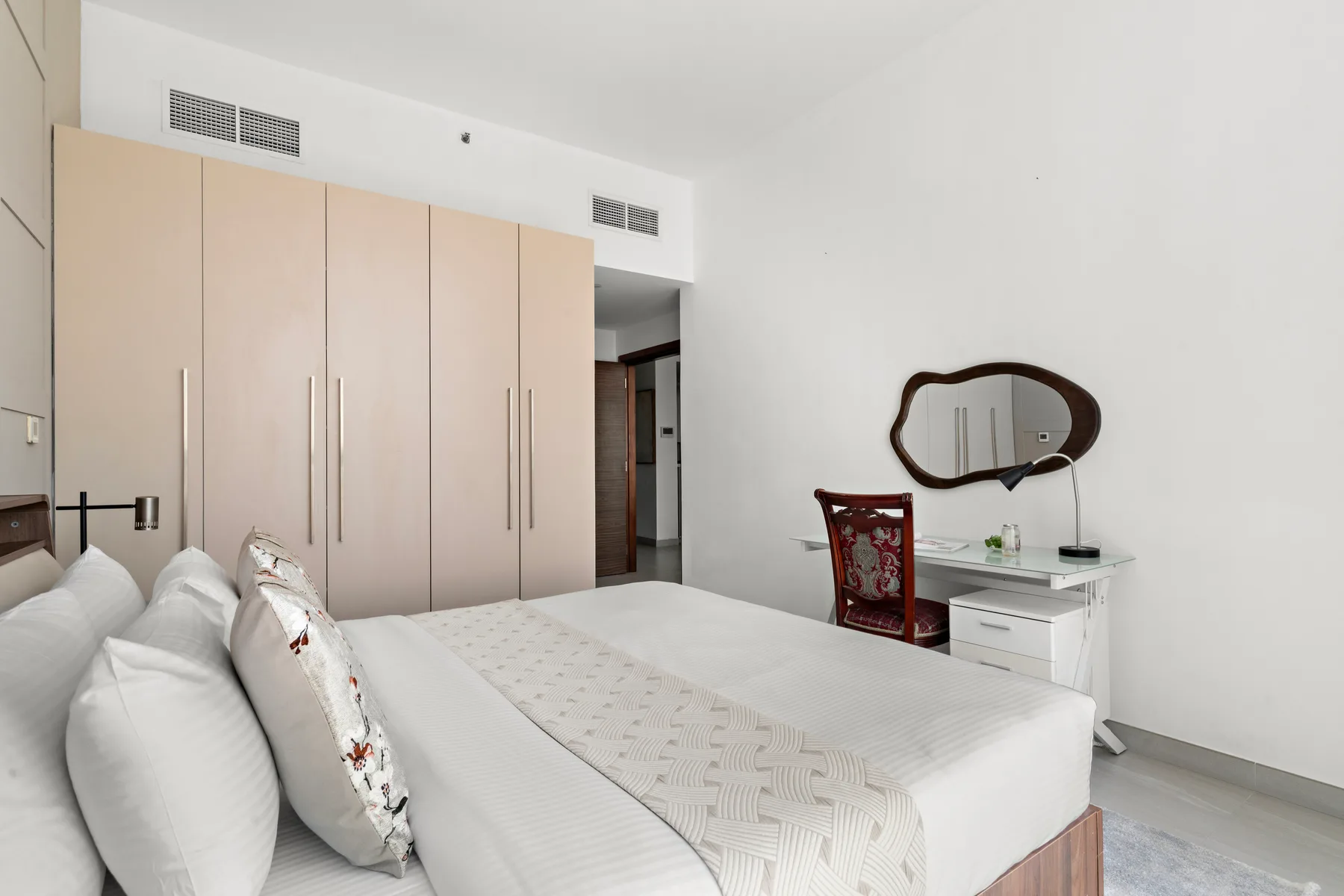 A bright bedroom with a large bed, tall wardrobes, and a small writing desk.