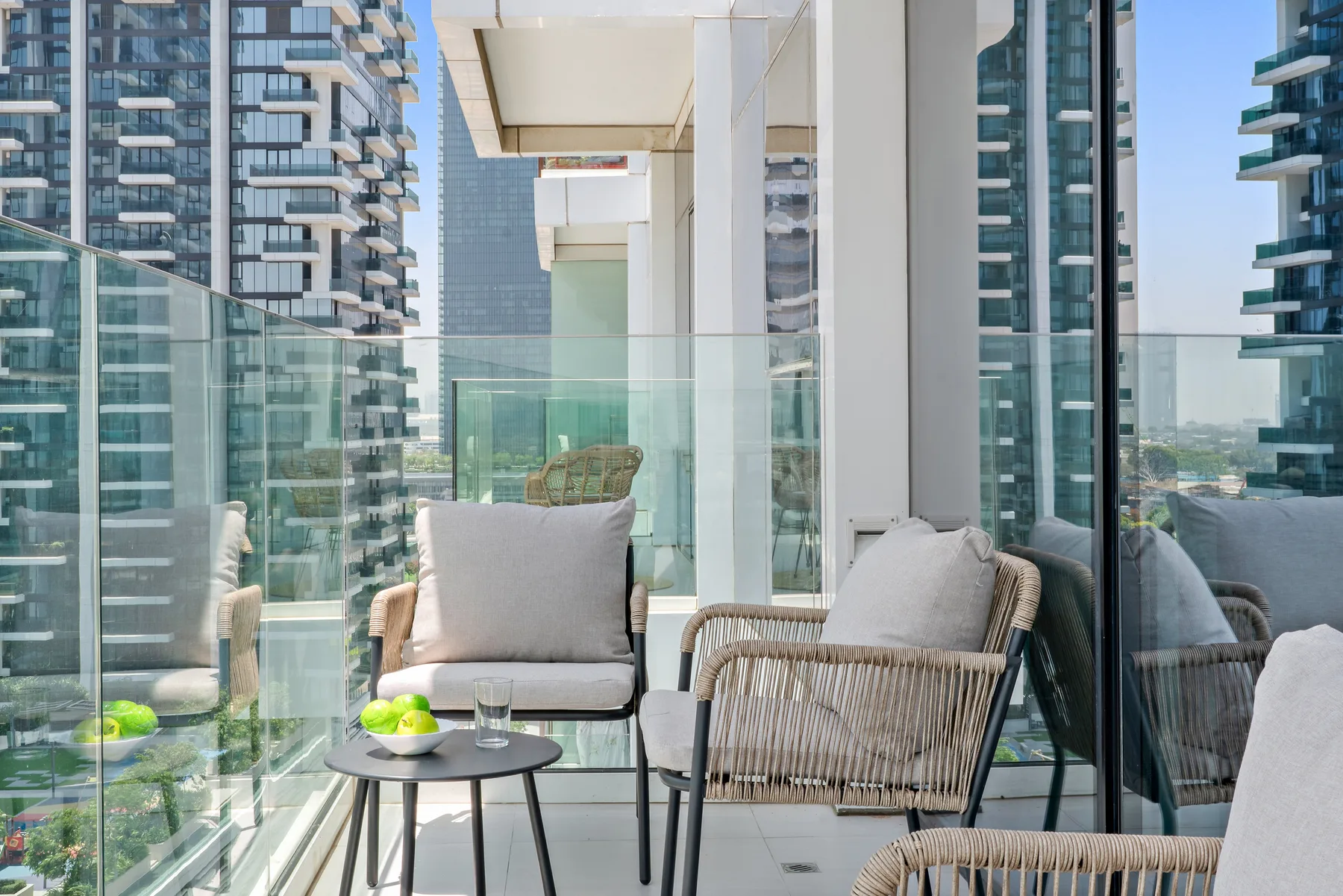 A balcony seating area with glass railings and views of nearby high-rise buildings.