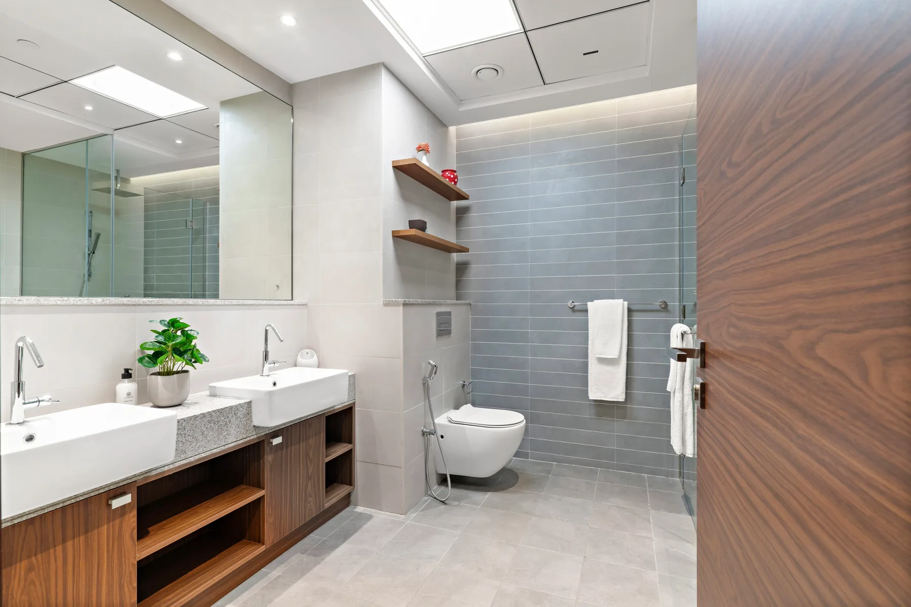 A modern bathroom with a long vanity, wall-mounted sink, and tiled shower area.