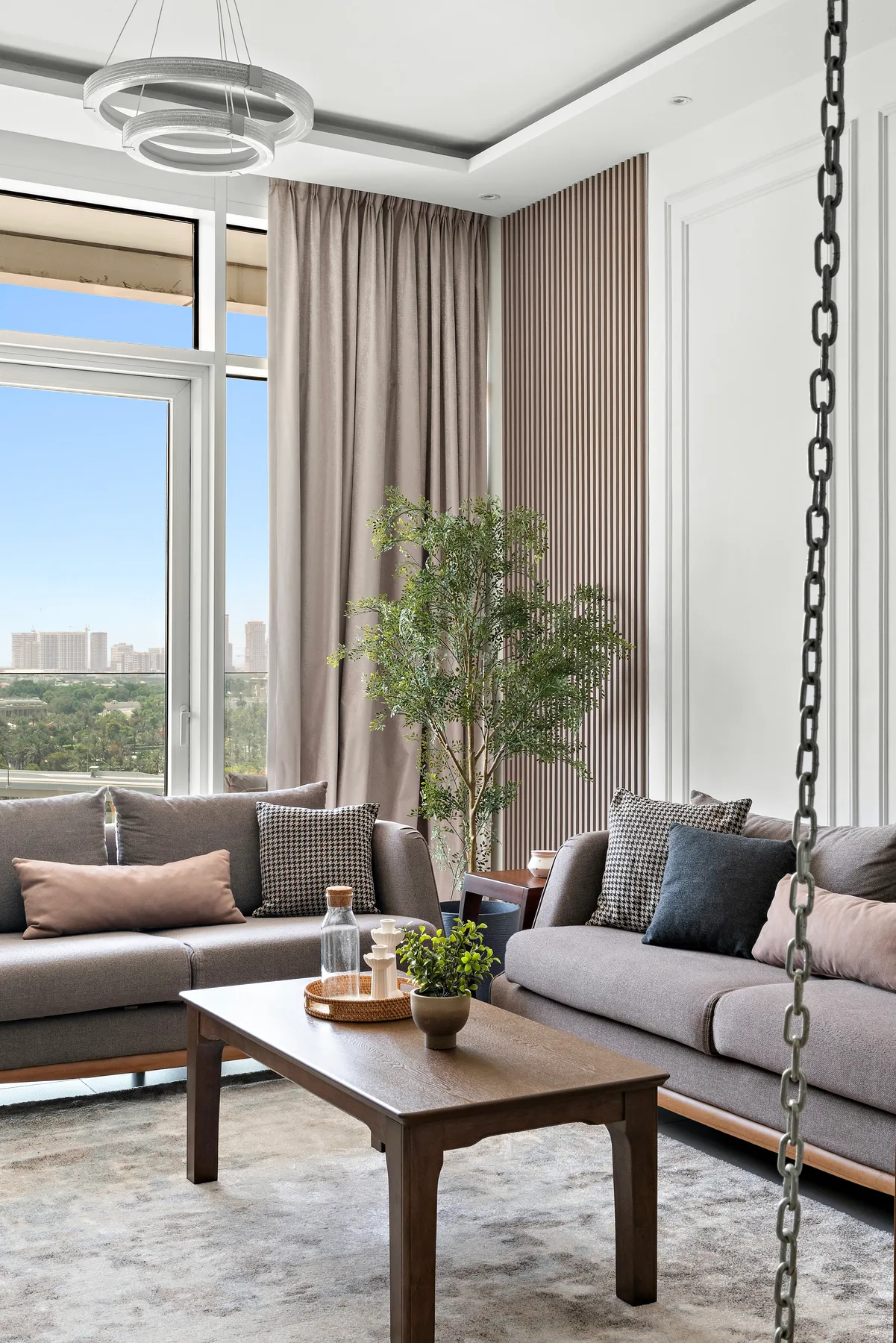 A bright living room with seating, a coffee table, and tall windows overlooking the city.