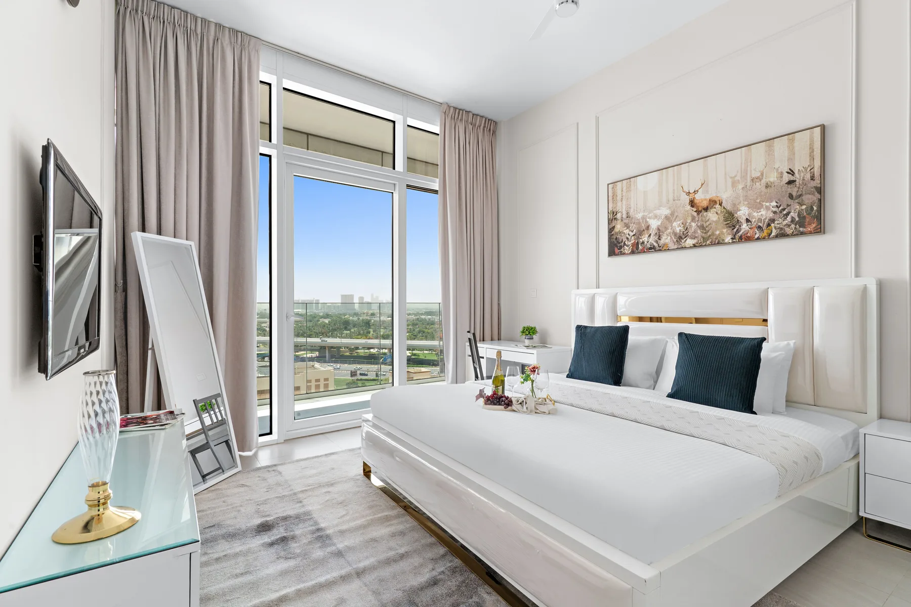A bright bedroom with a large bed beside floor-to-ceiling windows.