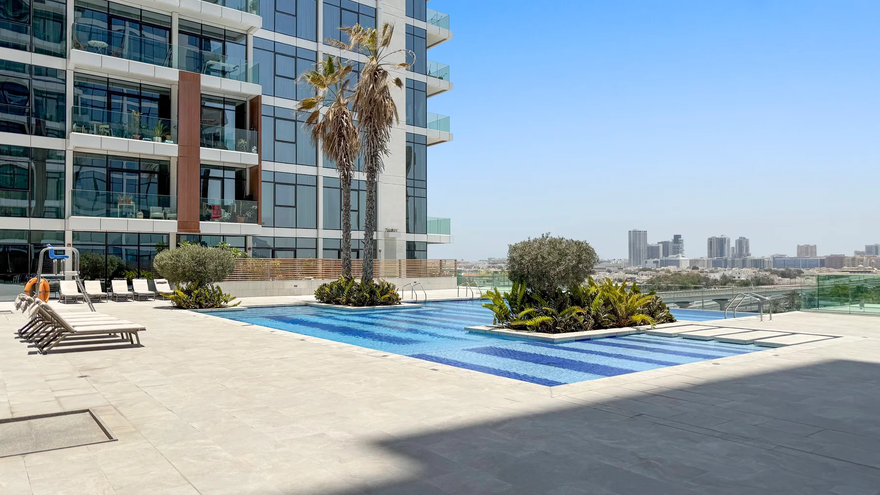 A rooftop pool beside a modern glass building, with lounge seating and planted areas.