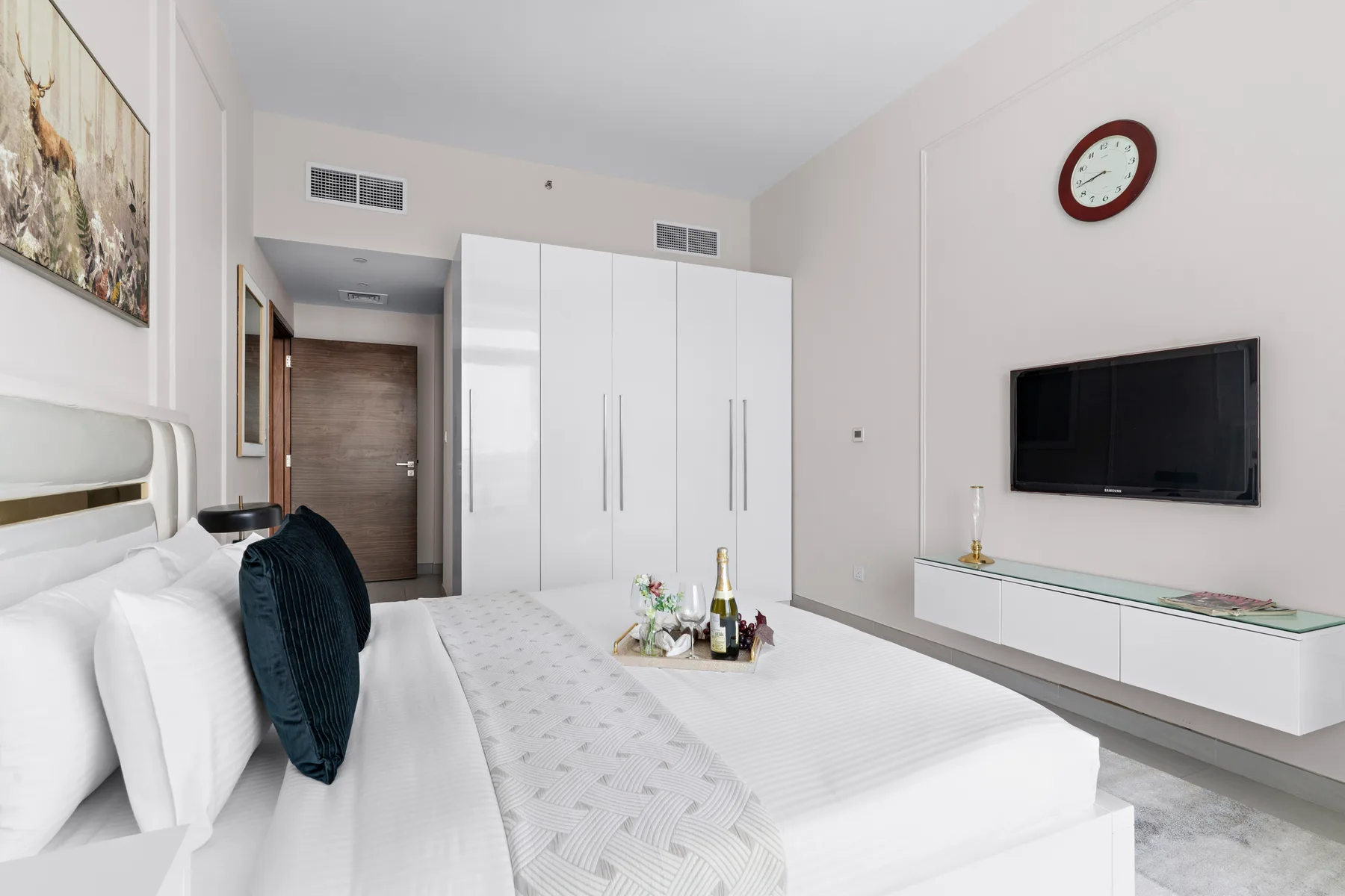 A bright bedroom with a bed, white wardrobes, and a wall-mounted television.