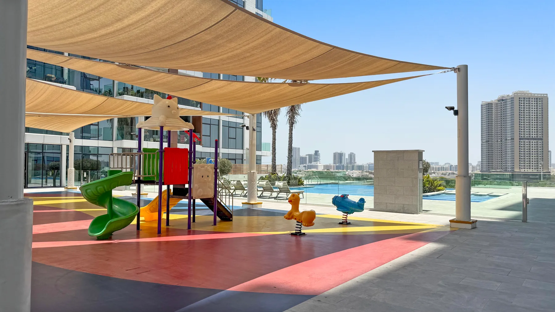 An outdoor playground with colorful play equipment sits beneath shade sails.