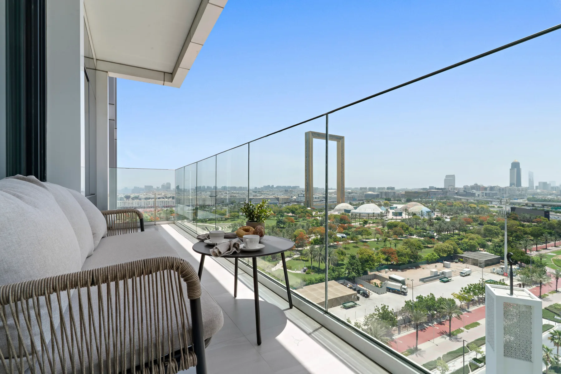 A balcony seating area overlooks a cityscape through a glass railing.