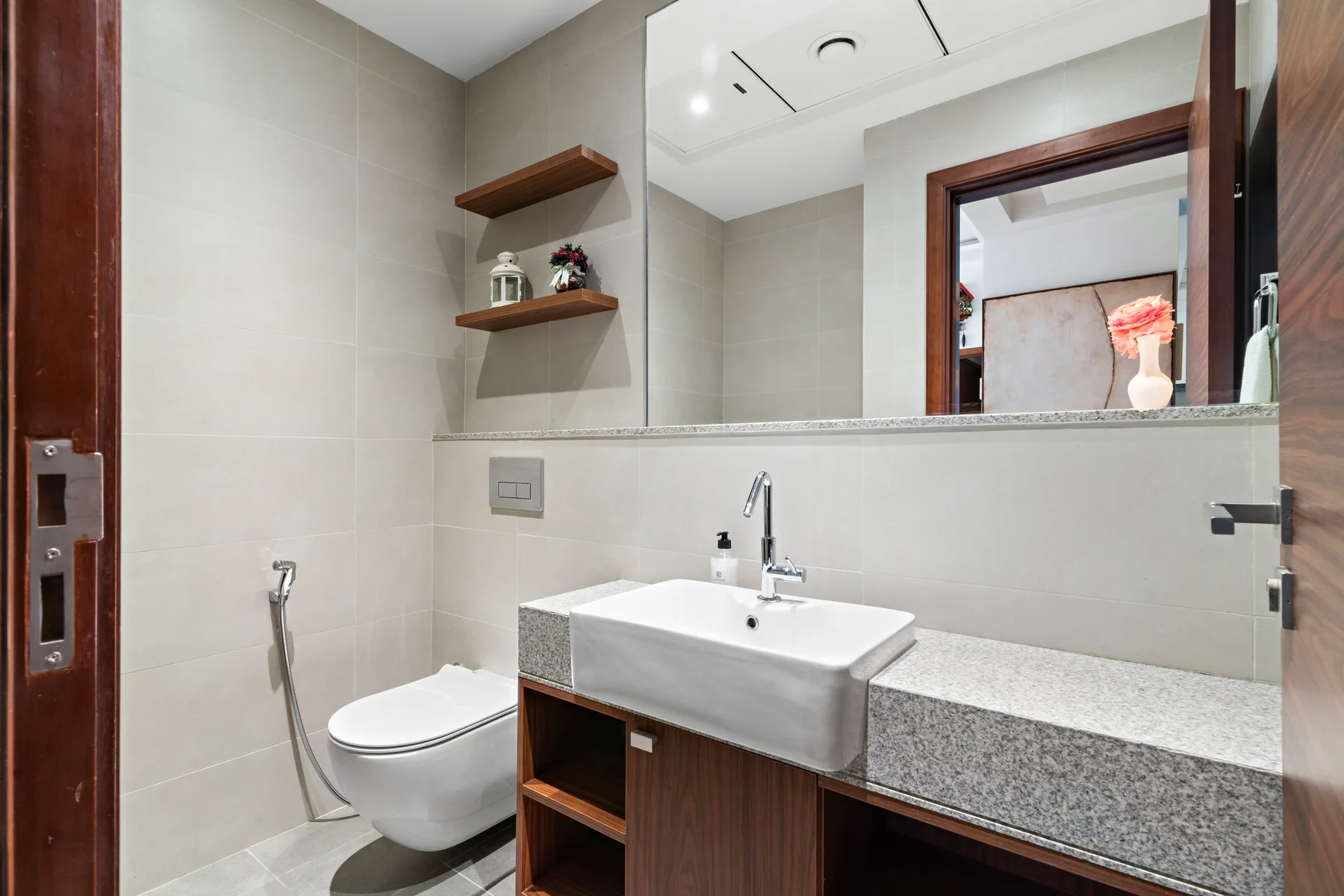 A tiled bathroom with a sink, toilet, and wide mirror.