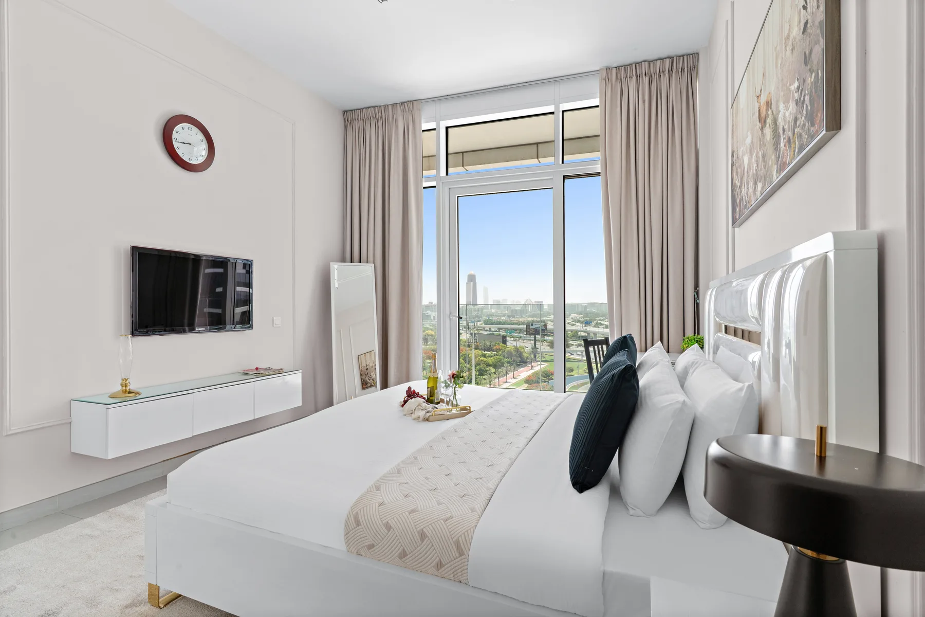 A bright bedroom with a large bed and tall windows overlooking the city.