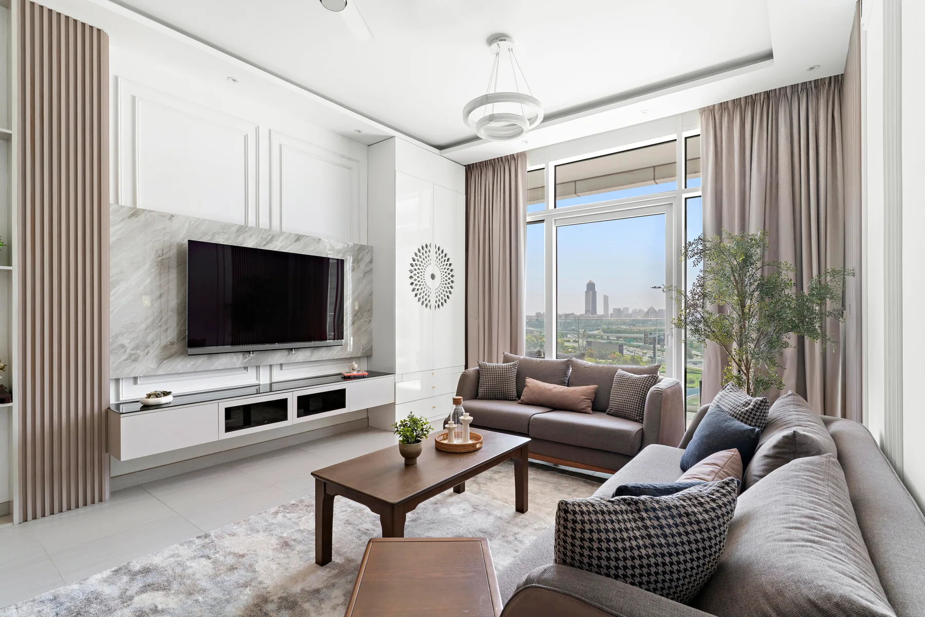 A bright living room with seating, a television, and large windows overlooking the city.