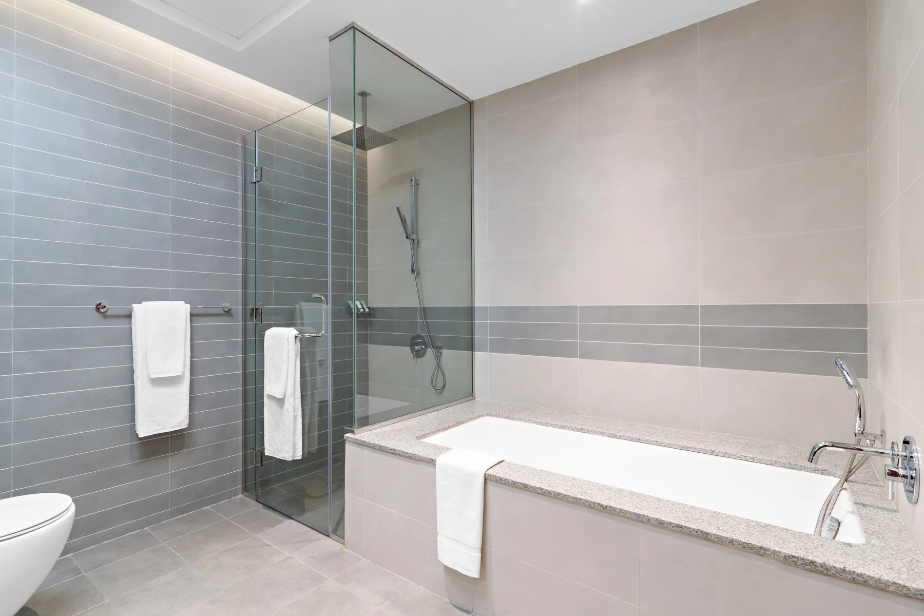 A modern bathroom with a bathtub, glass shower, and wall-mounted towels.