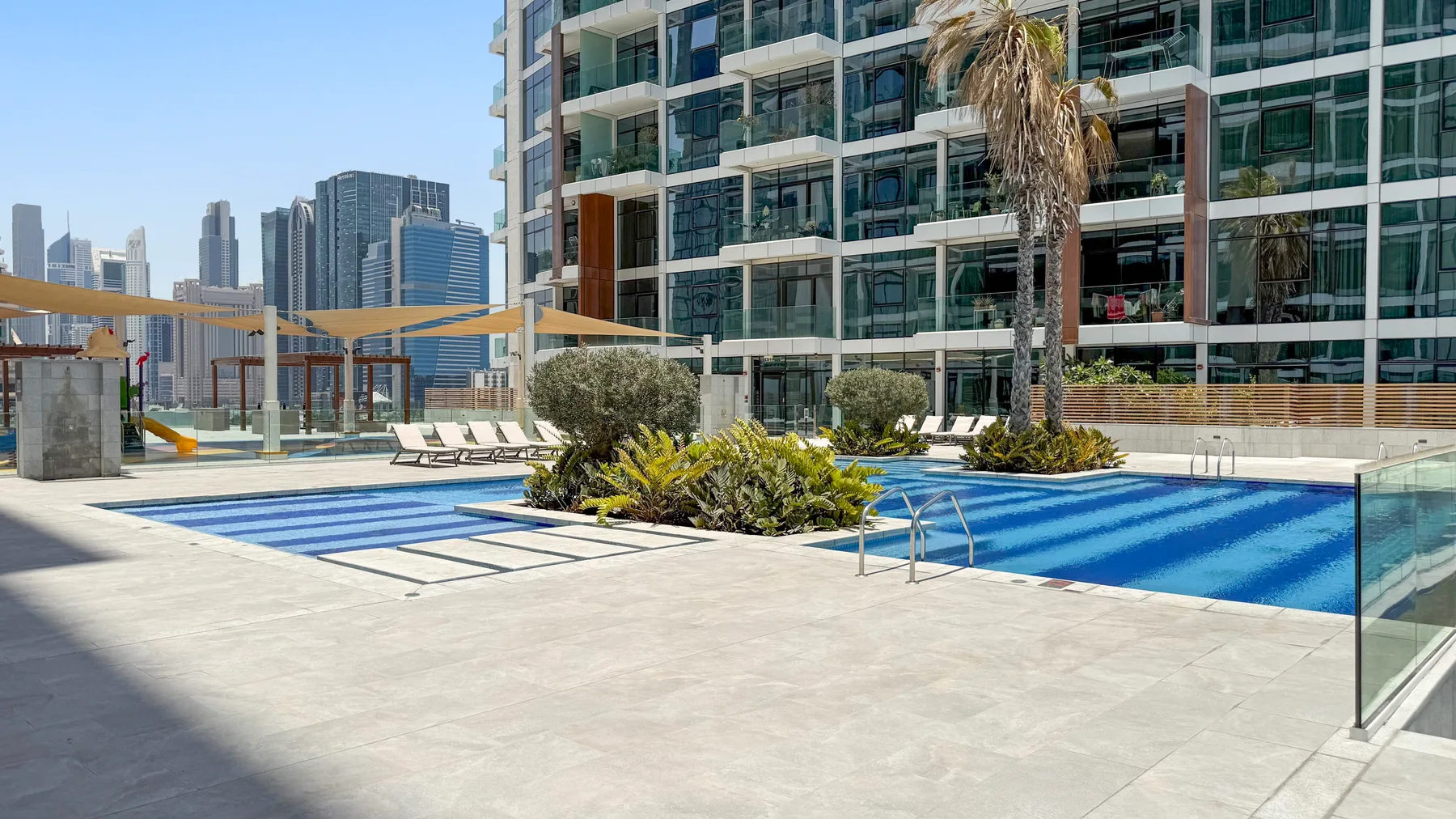 An outdoor swimming pool beside a modern glass-fronted building.