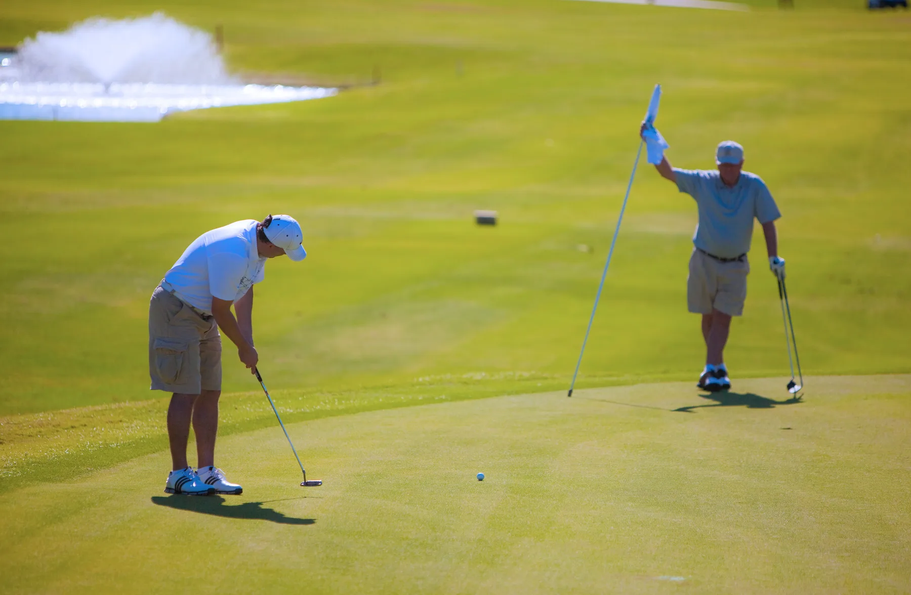 Dos golfistas juegan en un green, con una bandera cerca.
