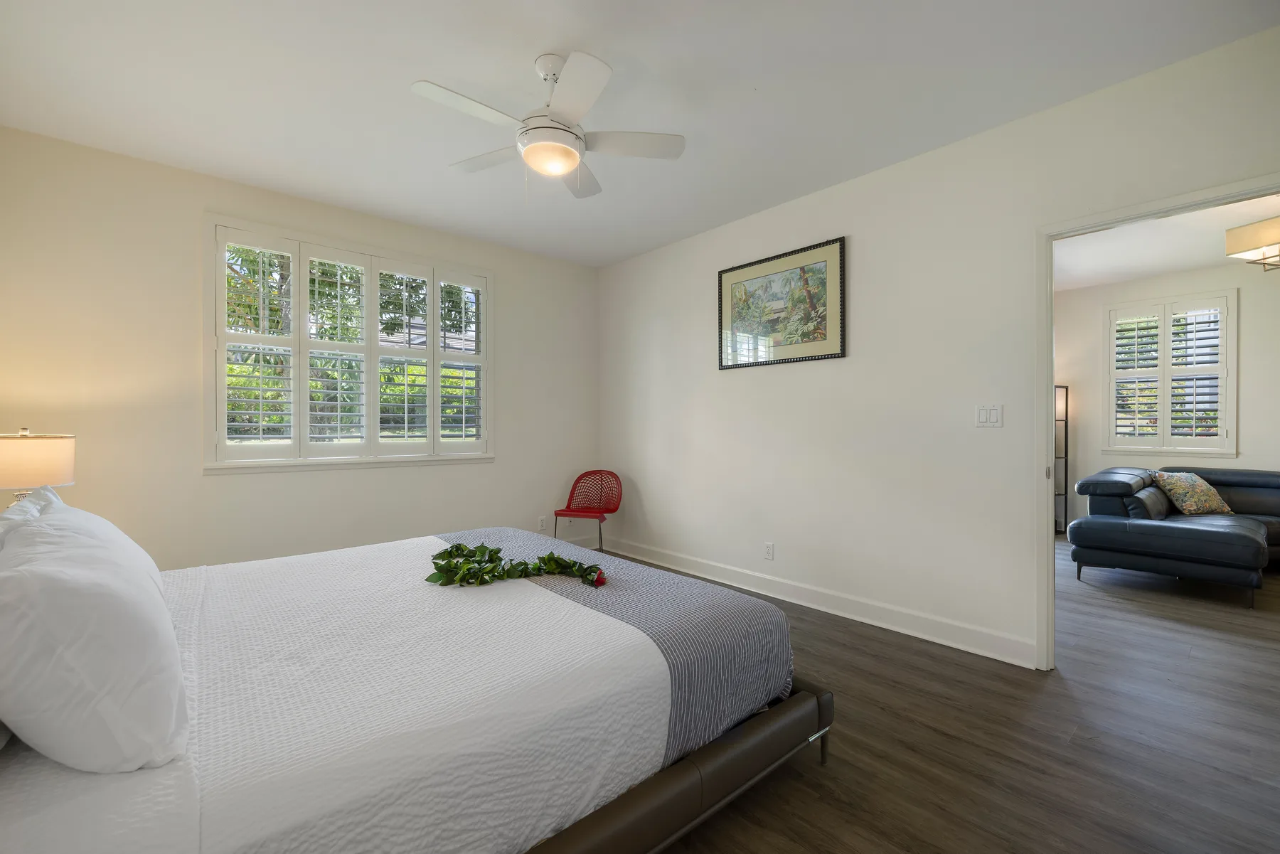 Un dormitorio con una cama bien tendida, un ventilador de techo y ventanas con vista a la vegetación.