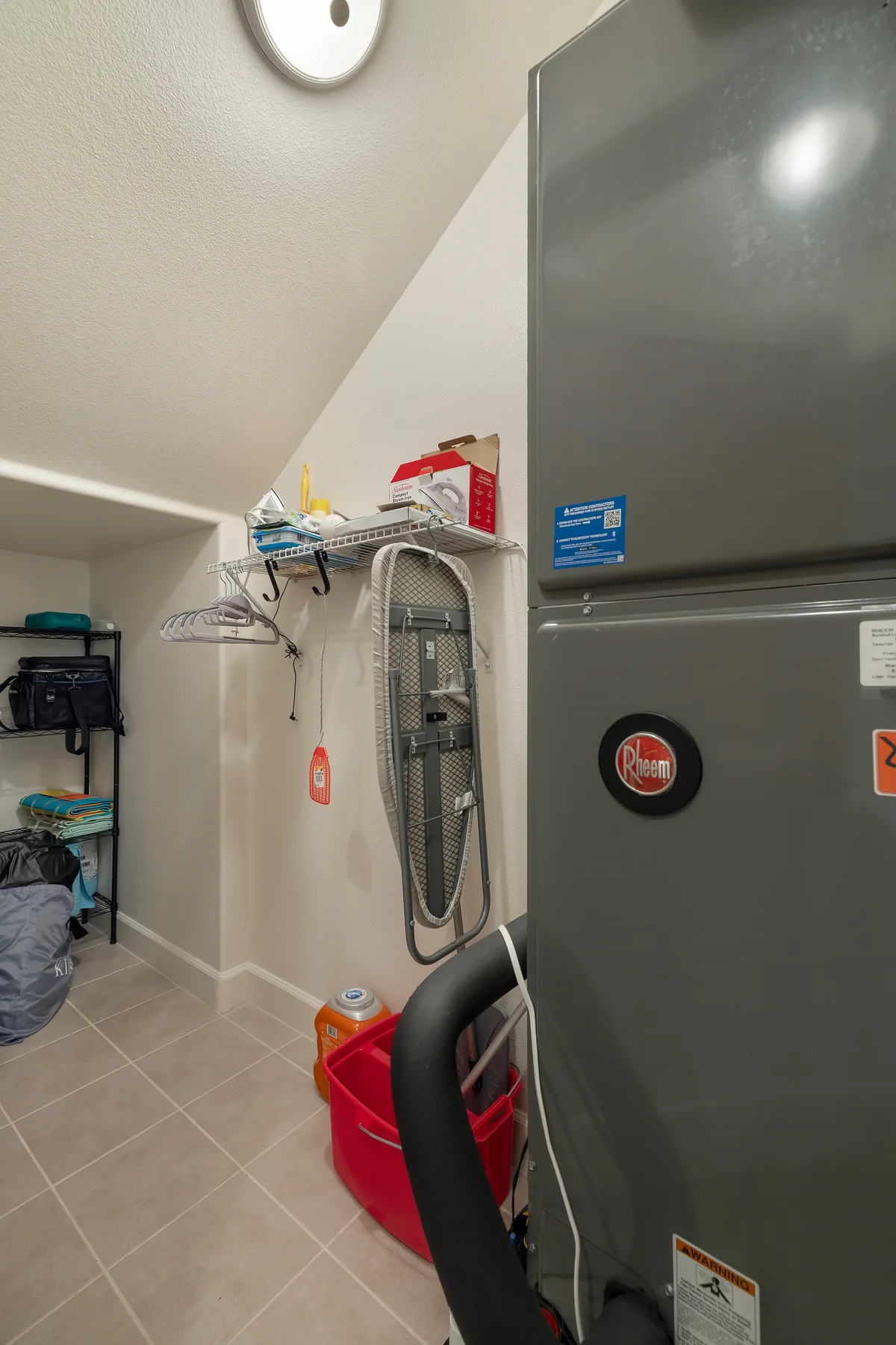 Una zona de lavandería con un refrigerador, una tabla de planchar y artículos de limpieza.