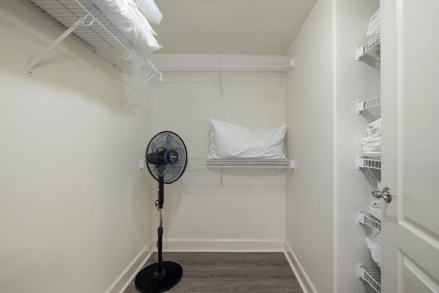Un vestidor con estantes de alambre y un ventilador de pie.
