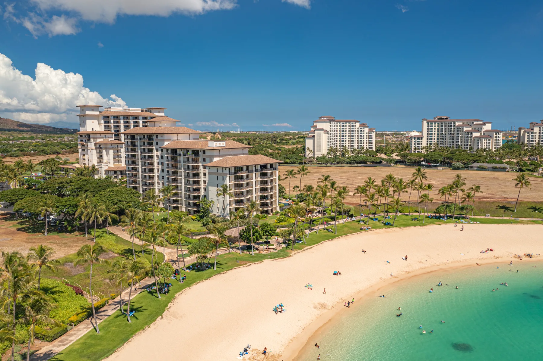 Edificios de un complejo junto a la playa dan a una playa de arena y aguas turquesas.