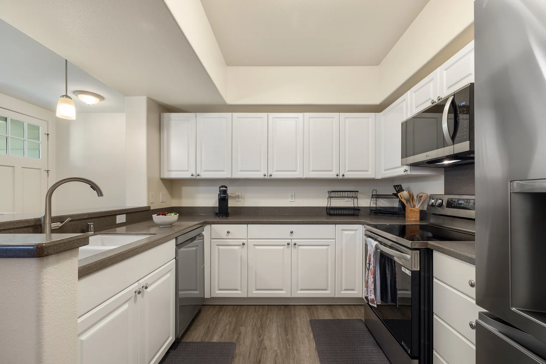 Una cocina luminosa con gabinetes blancos, encimeras oscuras y electrodomésticos de acero inoxidable.