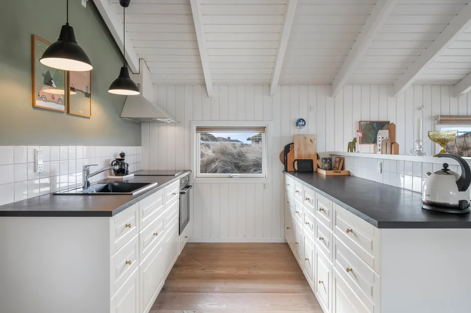 Una cocina luminosa con gabinetes blancos, encimeras oscuras y una ventana hacia el exterior.