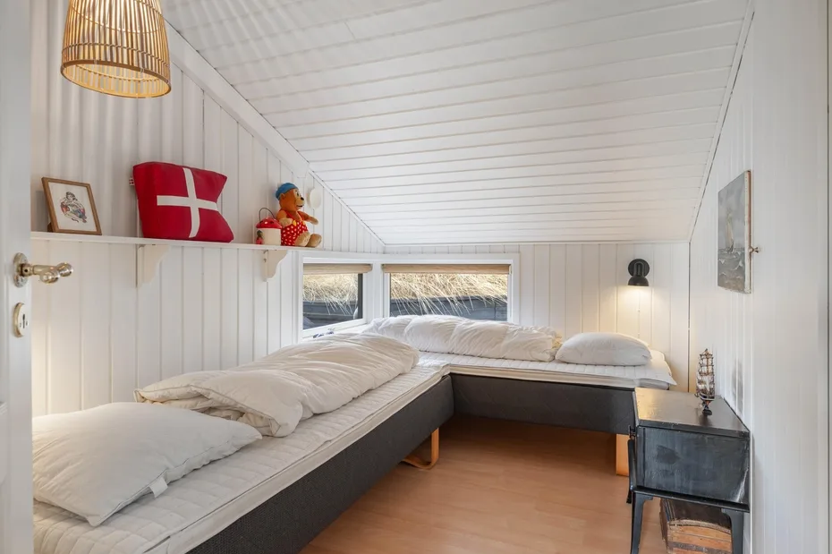 Un dormitorio abuhardillado y luminoso con camas bajo un techo blanco inclinado.