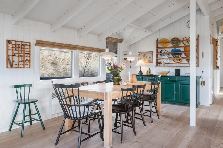 Comedor luminoso con una mesa de madera junto a una cocina verde azulado.