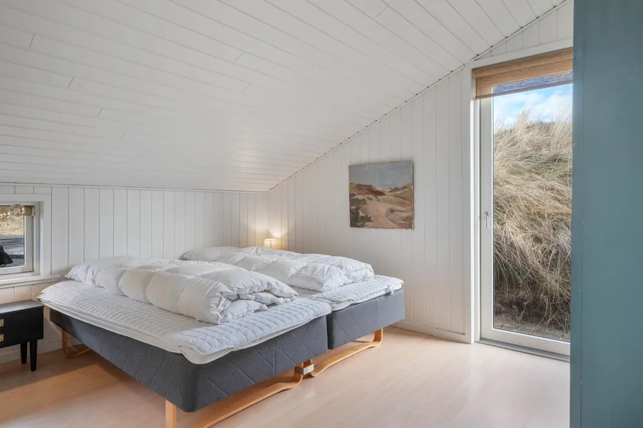 Un dormitorio luminoso con dos camas bajo un techo blanco inclinado.