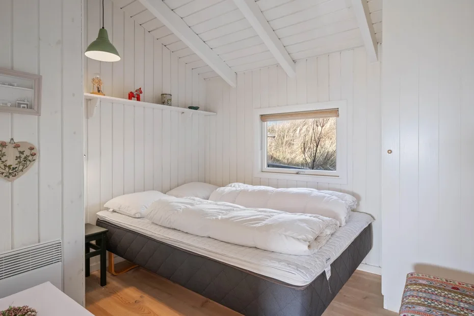Un dormitorio luminoso con una cama amplia bajo un techo blanco inclinado.