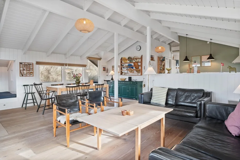 Una luminosa sala y comedor de concepto abierto, con un sofá negro y una mesa de comedor alargada.