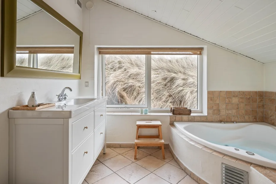 Un baño luminoso con bañera, lavabo y ventanas grandes.