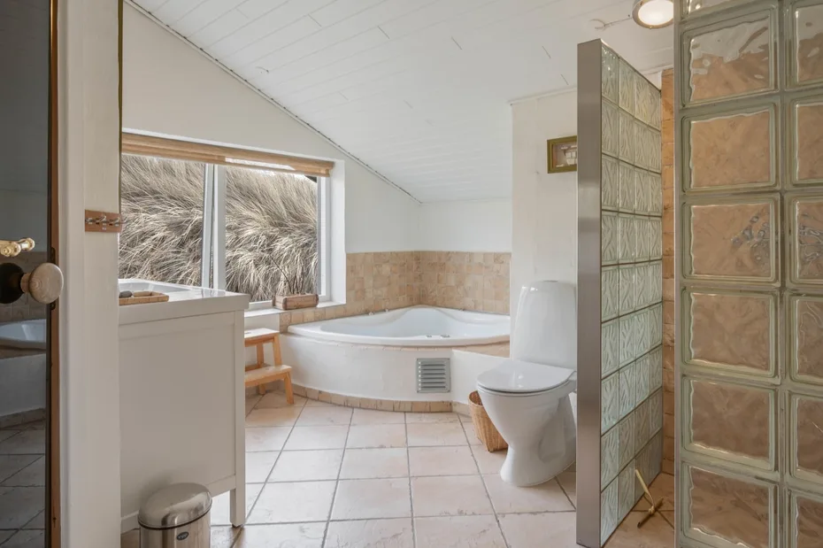 Un baño con bañera de esquina, inodoro y separador de bloques de vidrio.
