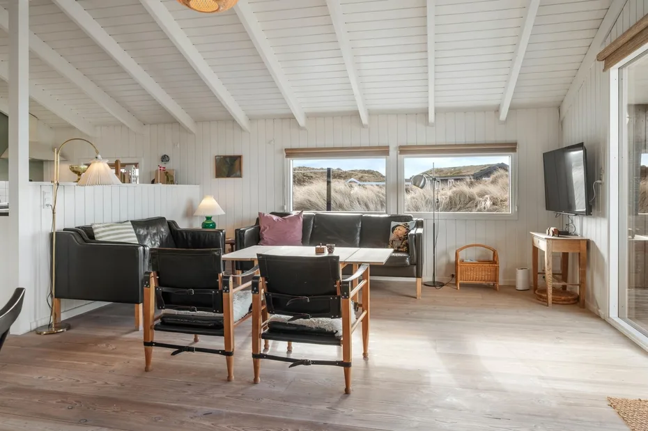Una sala luminosa con asientos, una mesa de comedor y ventanas con vistas a un paisaje rocoso.