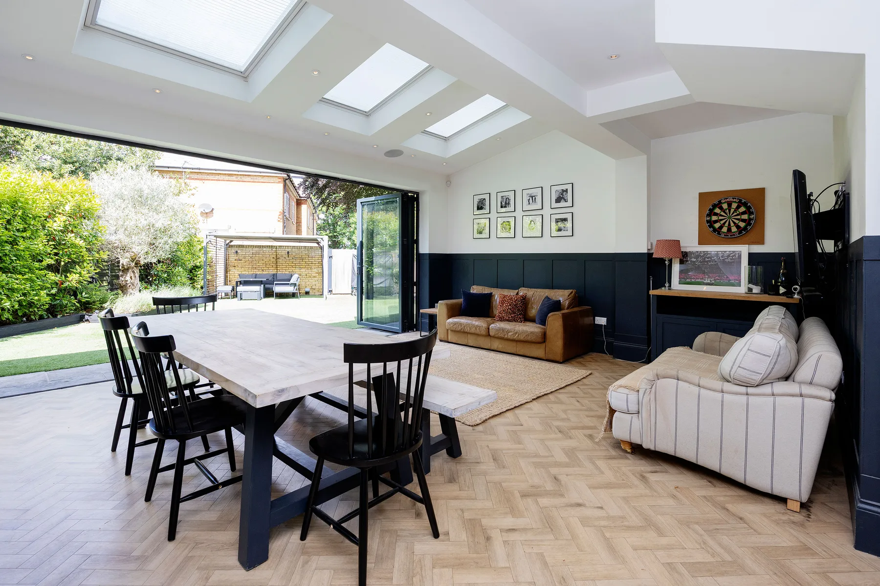 A bright open-plan living and dining area with skylights and doors opening onto a garden.