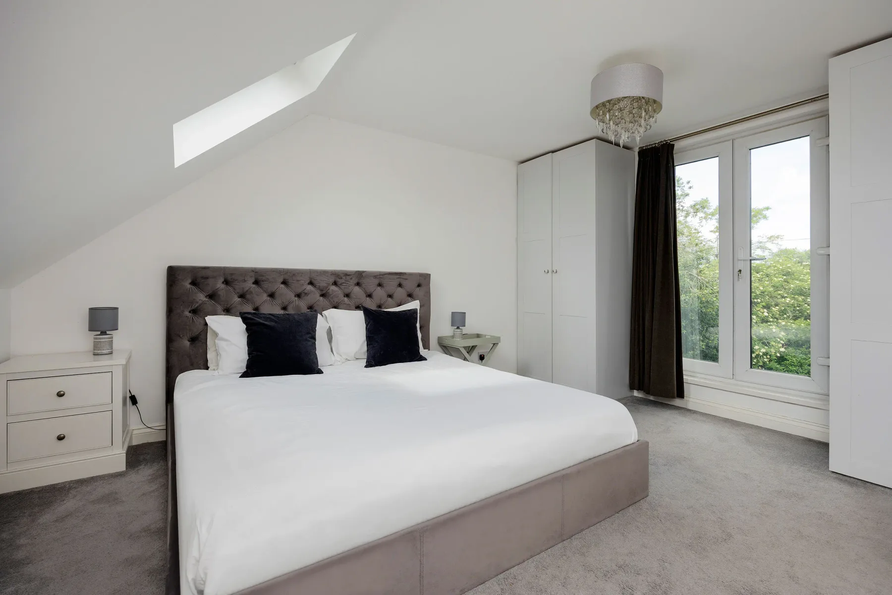 A bright bedroom with a large bed and tall windows overlooking greenery.