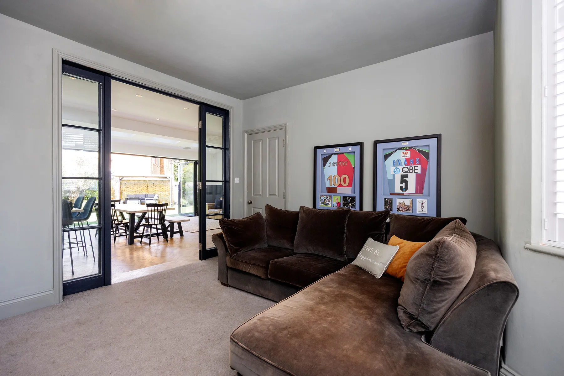 A living room with a brown sectional and framed sports memorabilia on the wall.