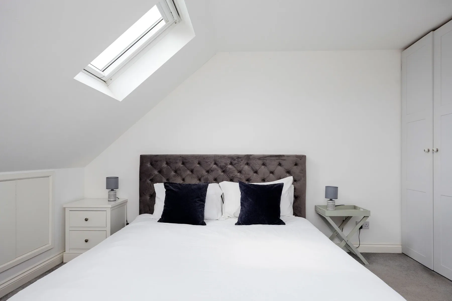 A bright bedroom with a bed beneath a sloped ceiling and skylight.