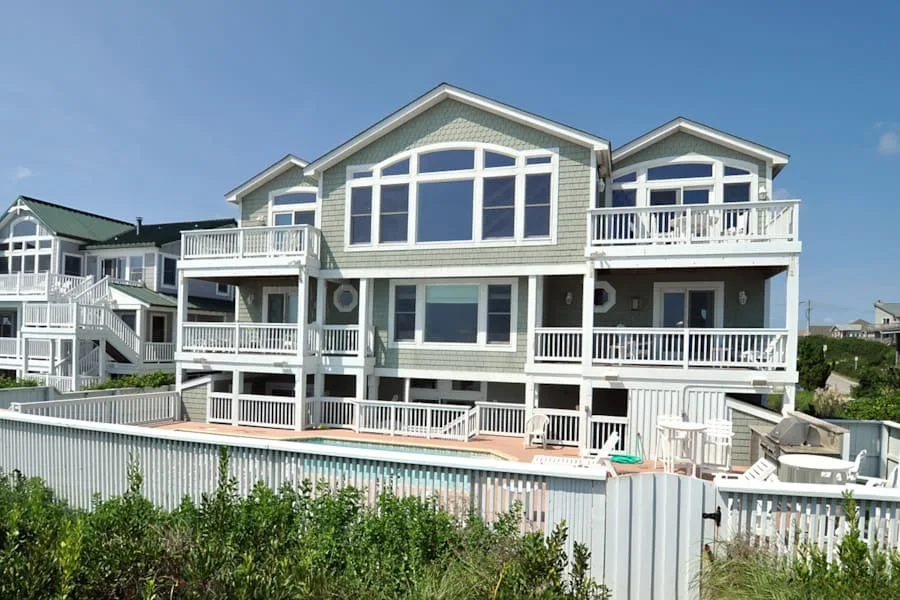 Una casa grande de estilo costero con balcones está junto a una piscina exterior.